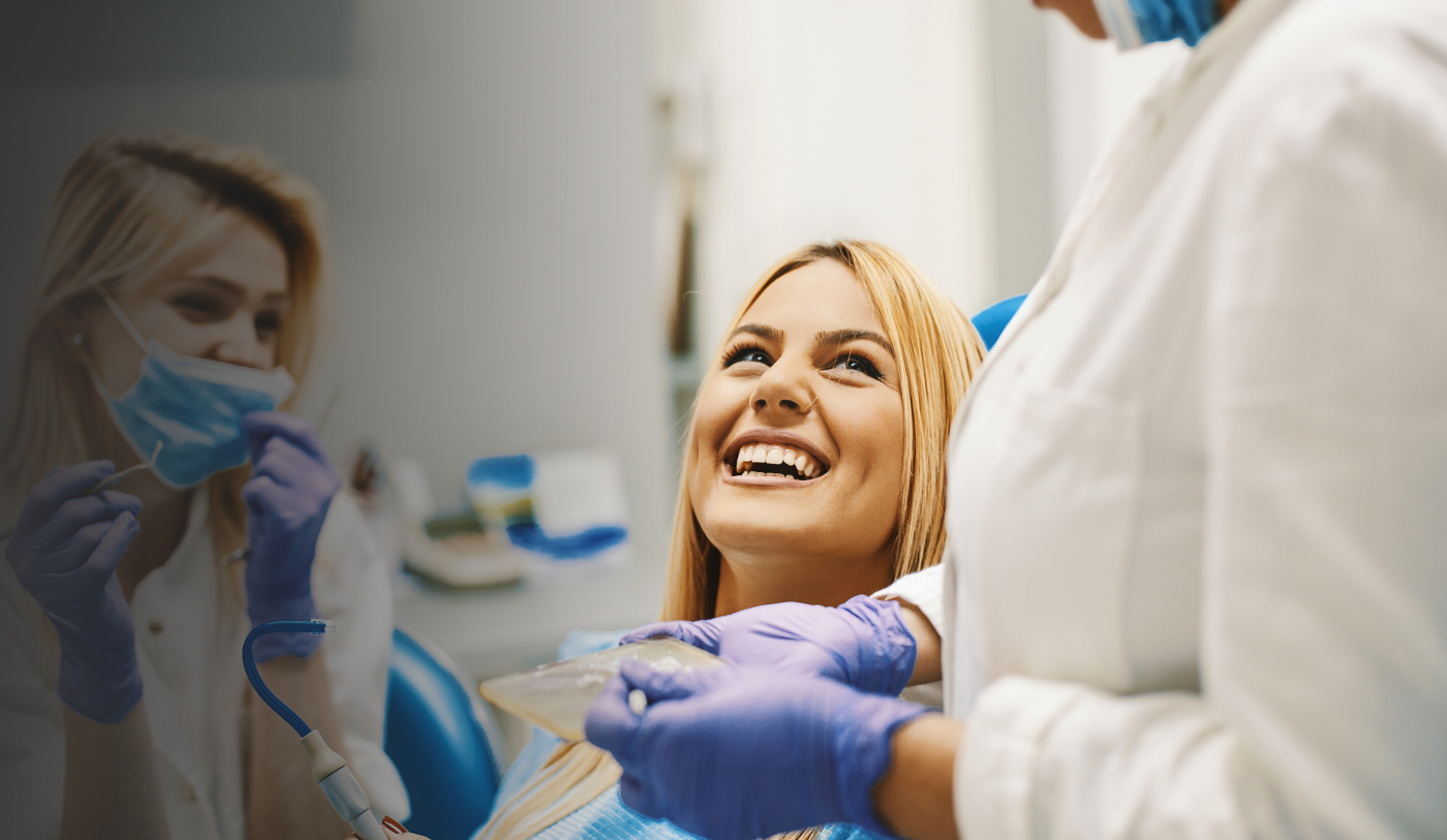 Woman in dental chair grinning up at her dentist